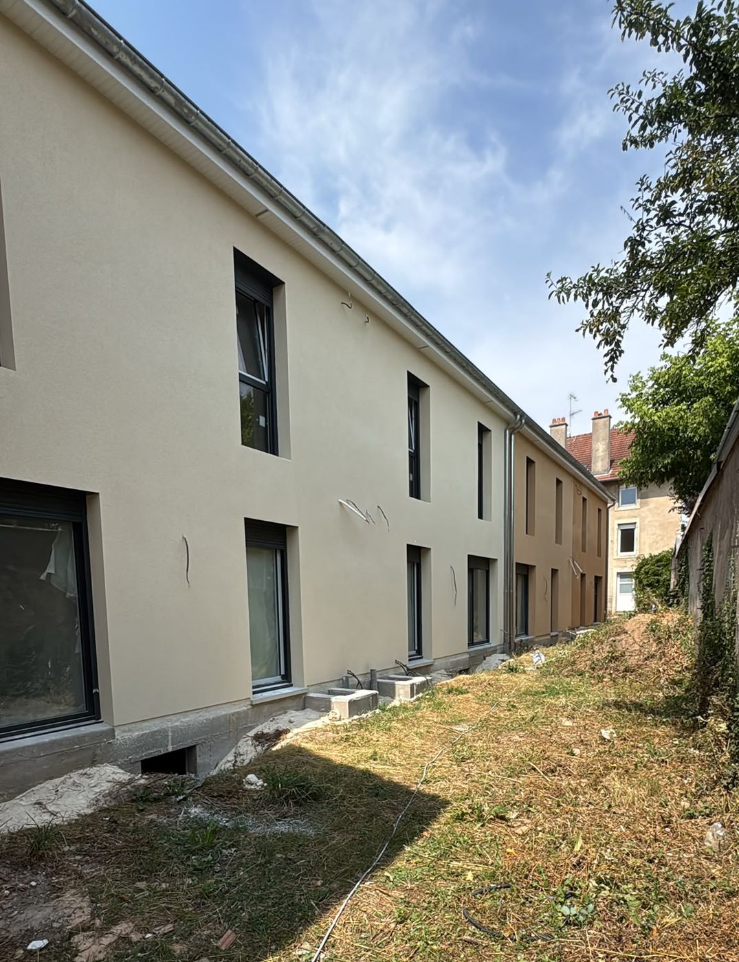 Longue façade de logements en enduit beige après travaux par SARL BATIBO
